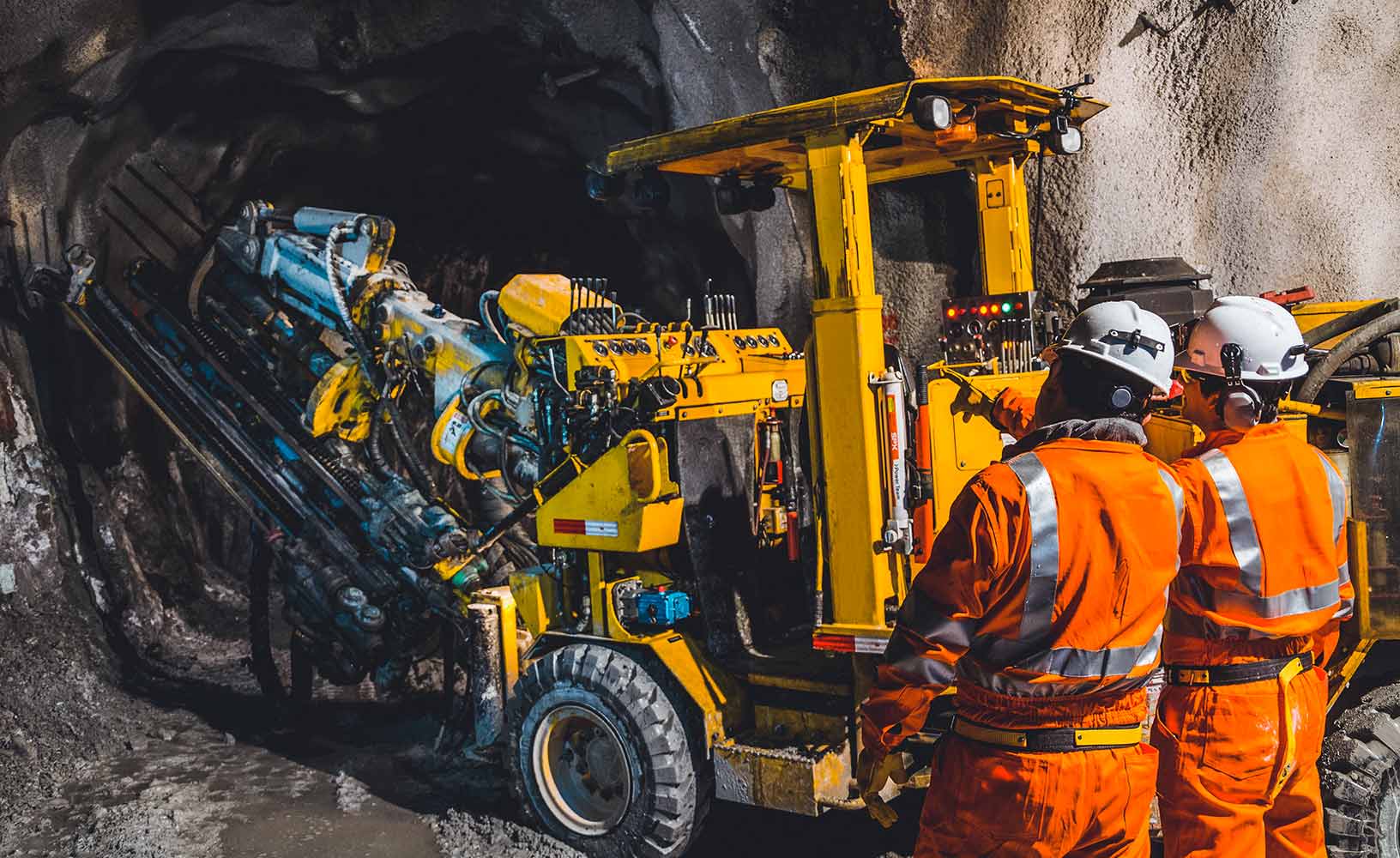 Two miners underground, in front of a mining machine